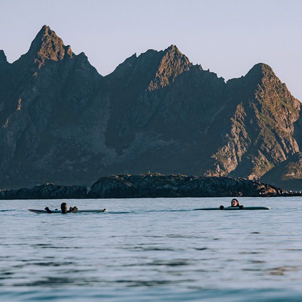 Picture of surfers out in the sea with mountains in the background
