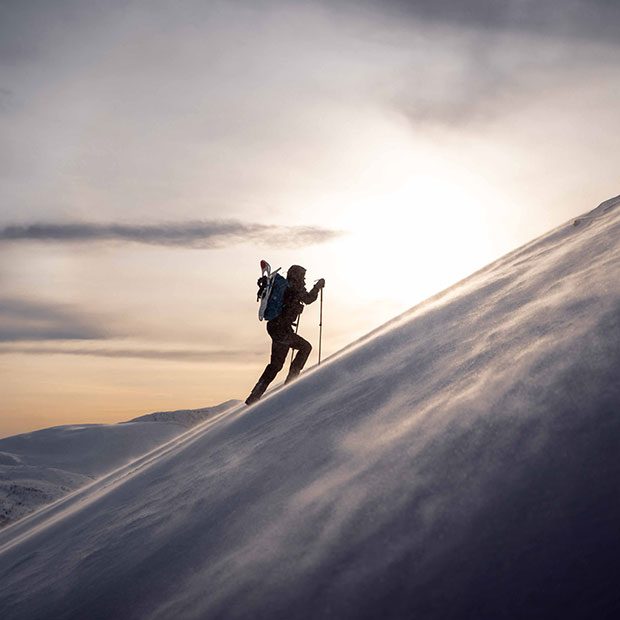Bilde av en person som går opp et fjell med staver på vinteren